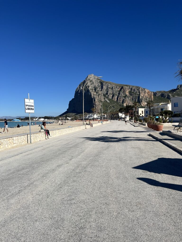 Strandpromenade von San Vito Lo Capo mit Blick auf den Monte Monaco, den Sandstrand und die Küste Siziliens bei sonnigem Wetter.
