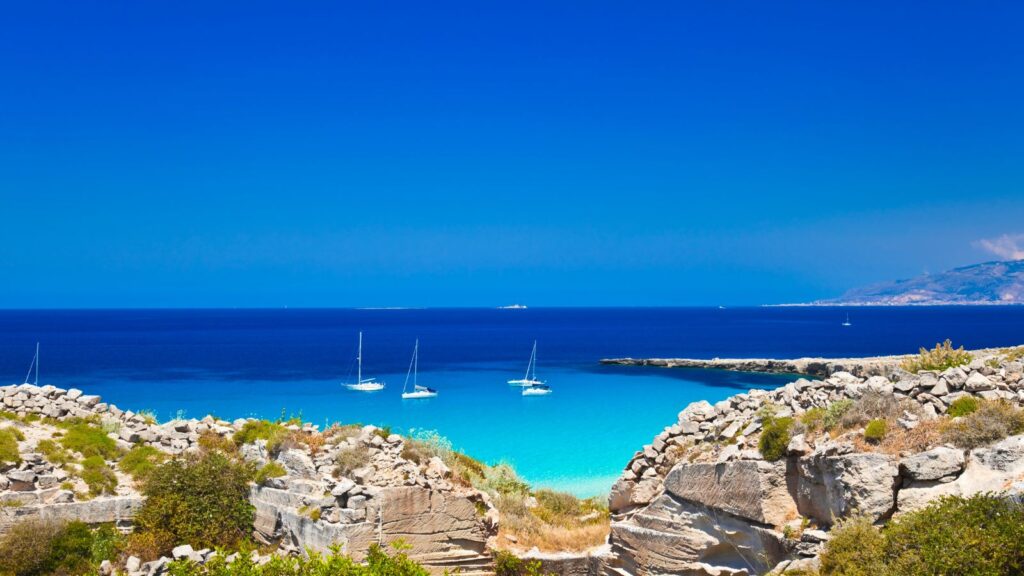 Türkisblaues Meer mit Segelbooten vor einer felsigen Küste auf den Ägadischen Inseln bei Favignana und Levanzo vor Sizilien.