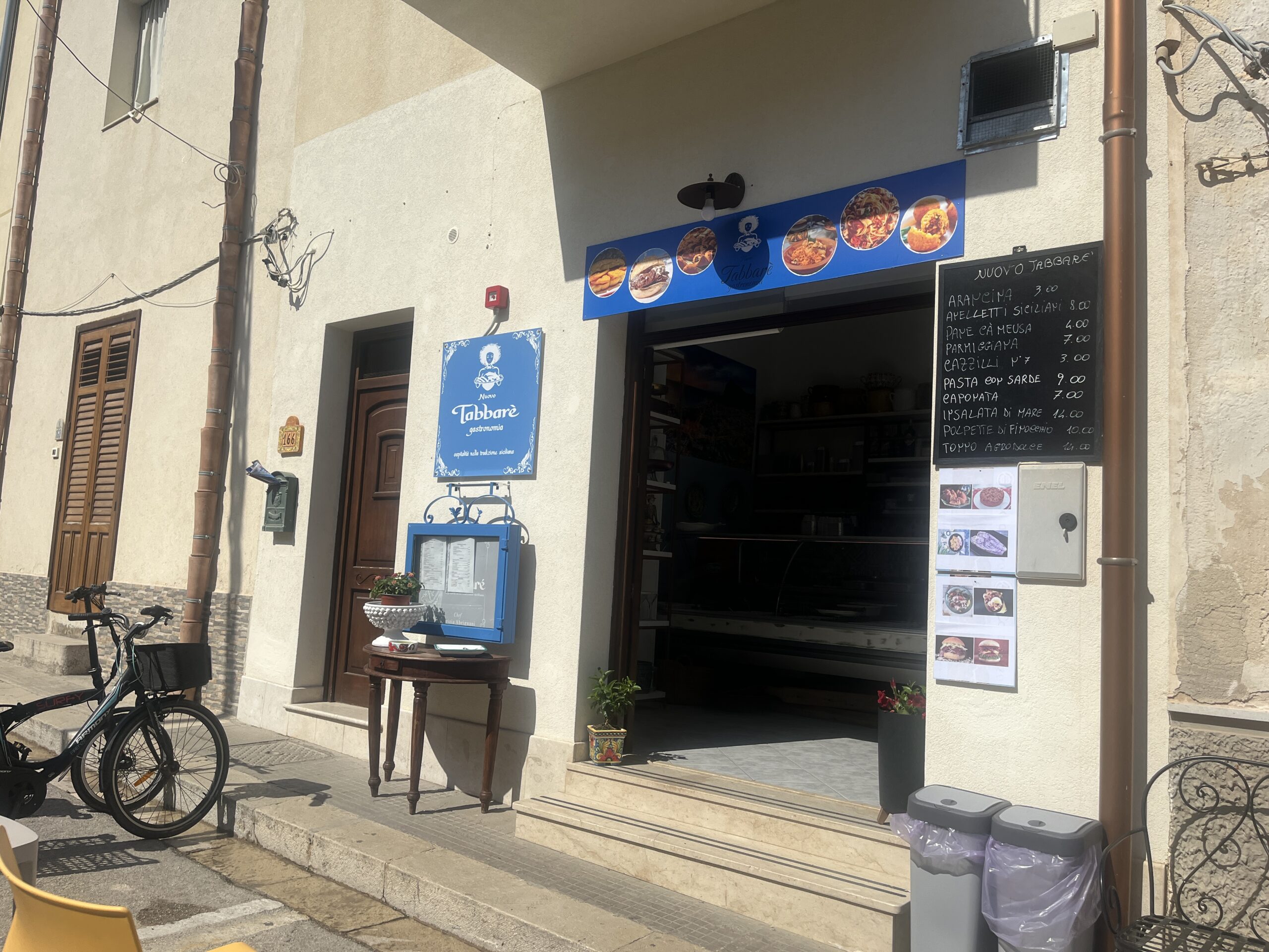 Eingang des Restaurants Nuovo Tabbare in San Vito Lo Capo mit Speisekarte vor dem Lokal und Sitzmöglichkeiten im Außenbereich.