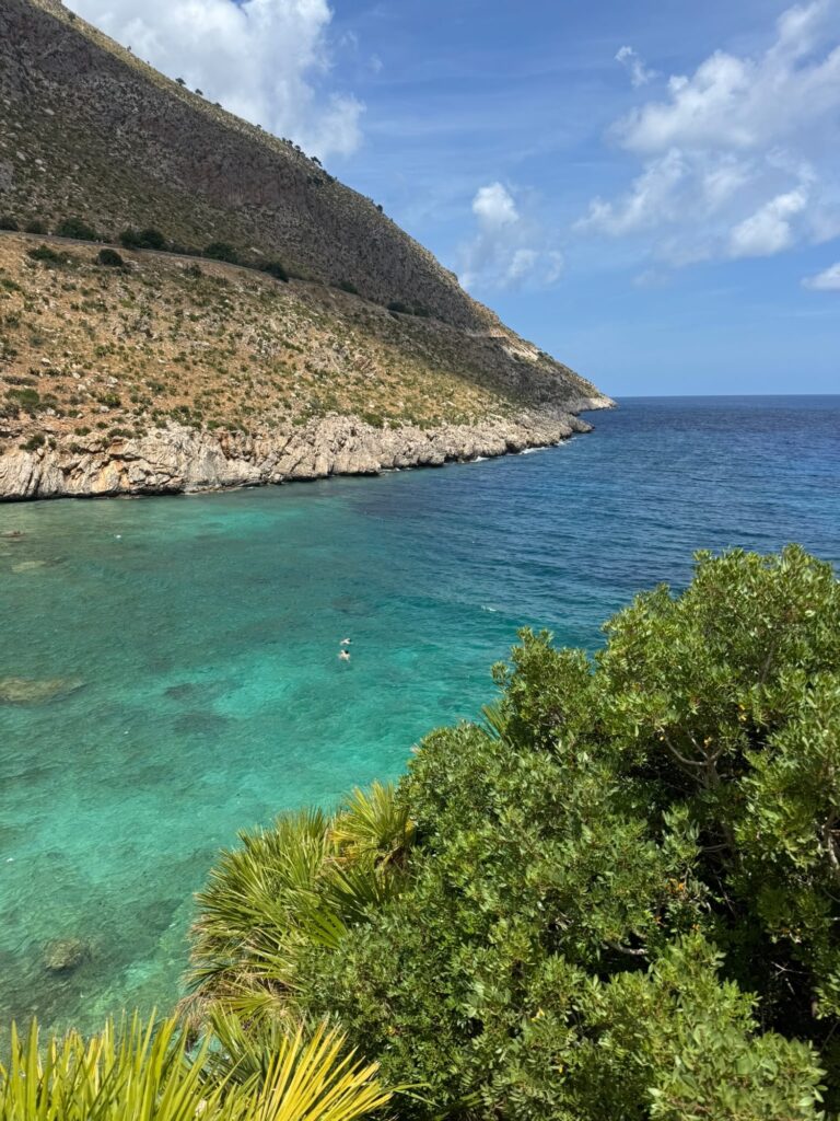 Türkisfarbene Bucht im Naturreservat Zingaro mit klarem Wasser, felsiger Küste, mediterraner Vegetation und steilen Berghängen im Hintergrund.