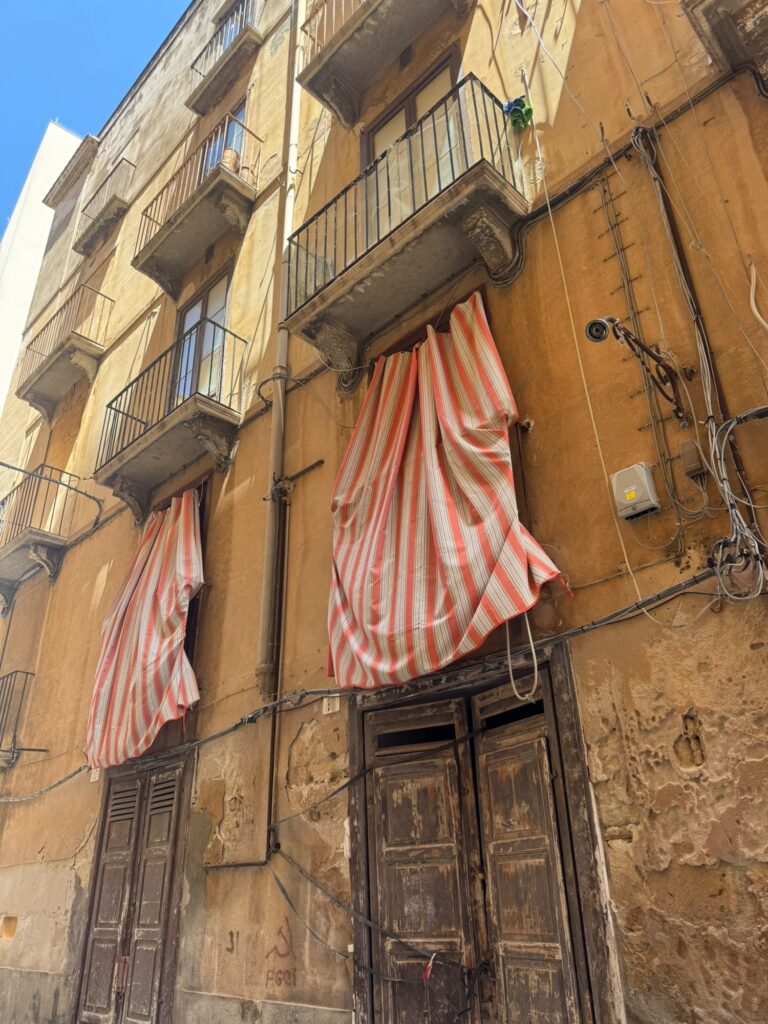Historisches Wohnhaus mit Balkonen, alten Türen und gestreiften Markisen in einer Gasse der Altstadt von Trapani auf Sizilien.
