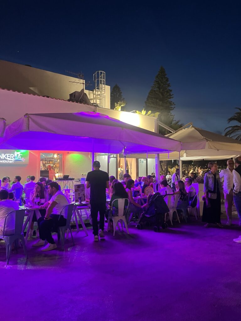 Gut besuchte Restaurantterrasse mit violetter Beleuchtung und zahlreichen Gästen in San Vito Lo Capo am Abend.