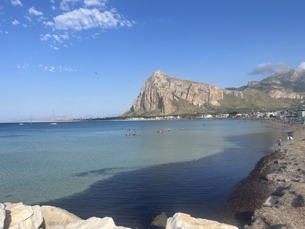 Panoramablick auf die Bucht von San Vito Lo Capo mit türkisblauem Meer, Sandstrand und dem markanten Monte Monaco im Hintergrund.