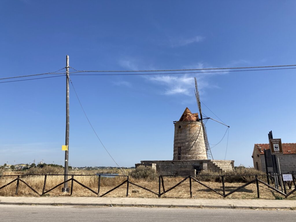 Historische Windmühle der Salinen von Trapani in Sizilien, umgeben von der traditionellen Salzlandschaft unter blauem Himmel.